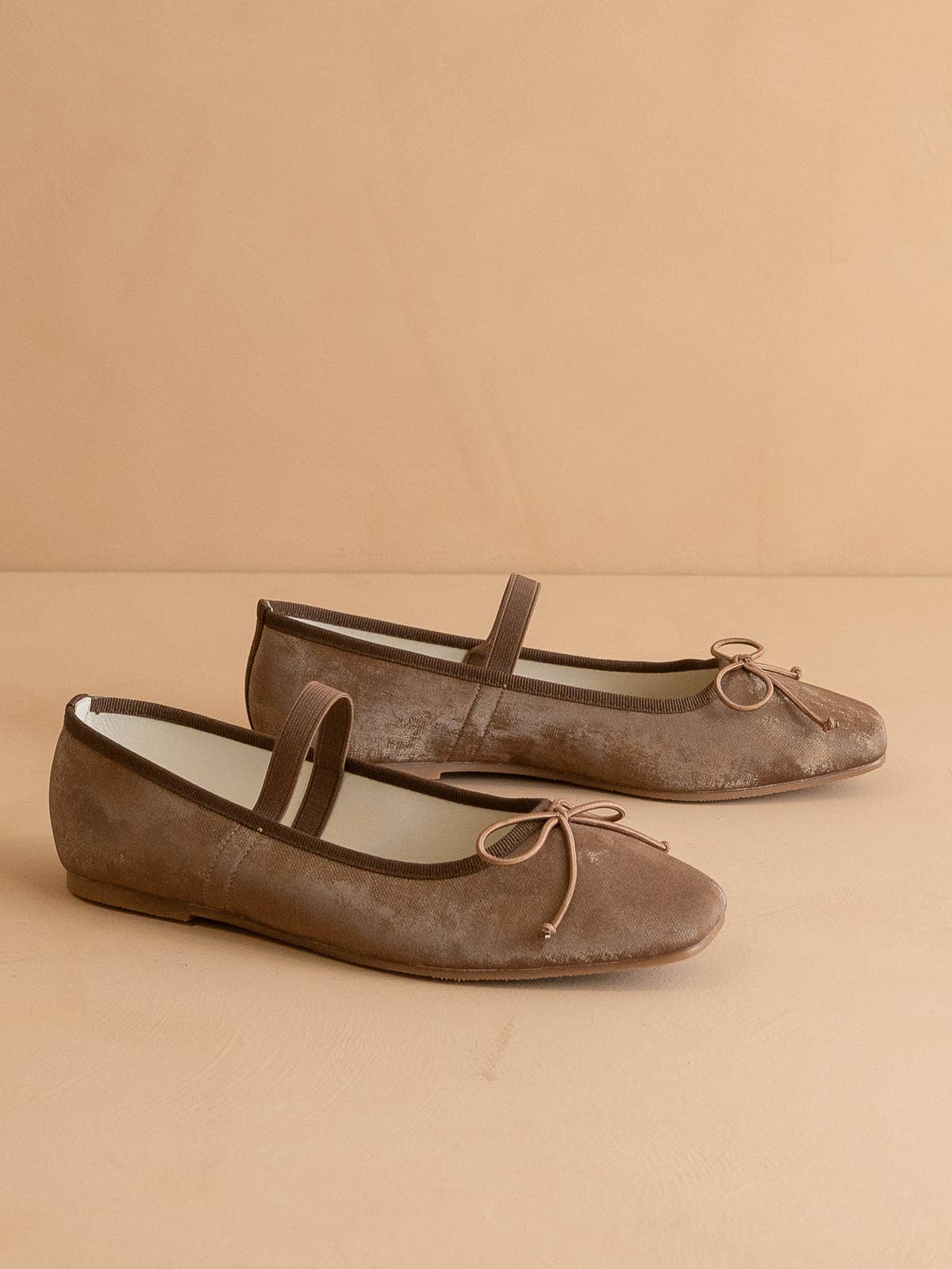 The OASIS SOCIETY London Ballet Flat features brown suede, rounded toes, front bows, and single straps—stylish Mary Jane slip-ons for everyday wear, shown on a neutral beige background.