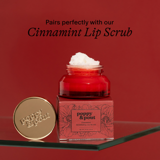 Red lip scrub jar with packaging and lid on a red background, featuring 'poppy & pout' branding.