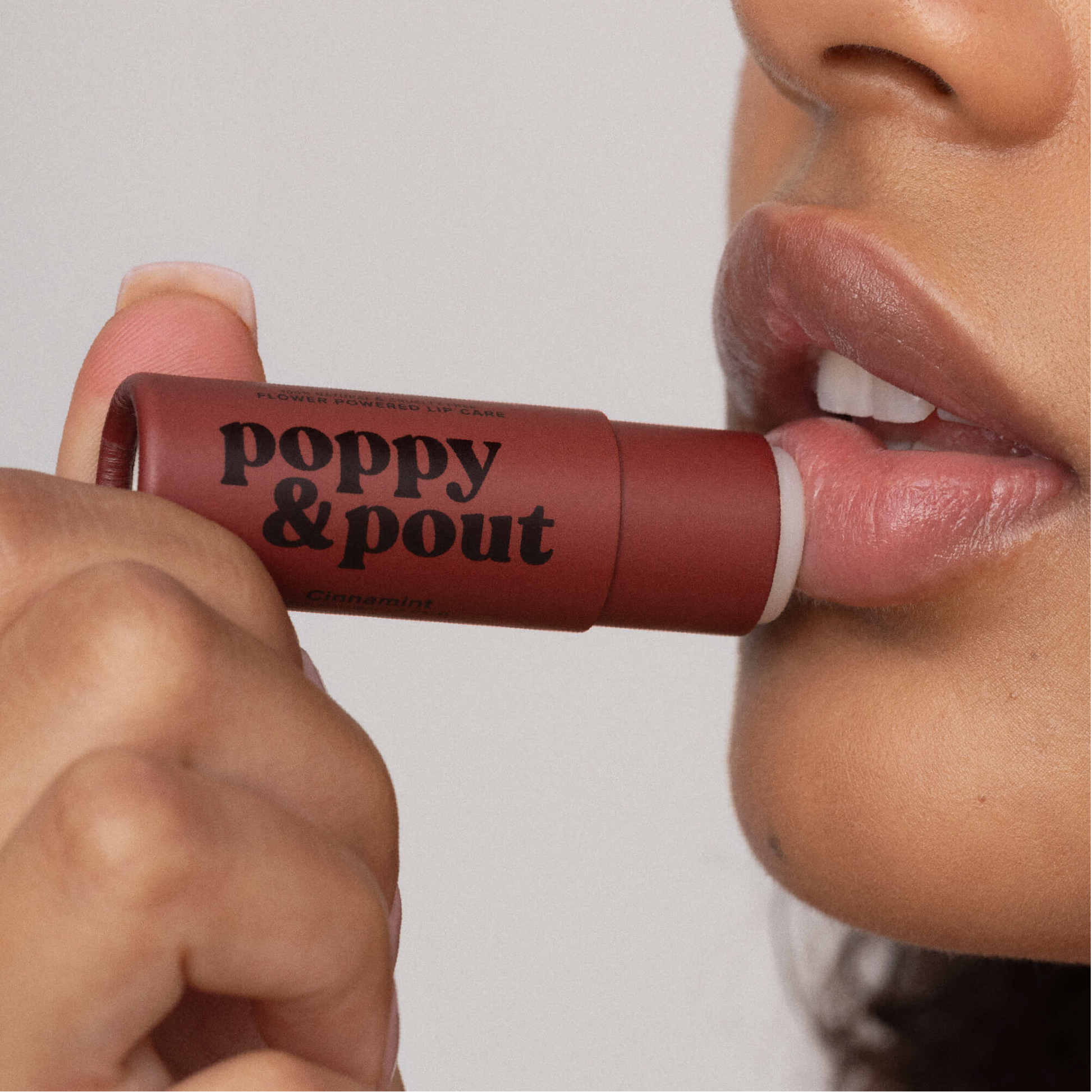 Person applying 'poppy & pout' lipstick to their lips.