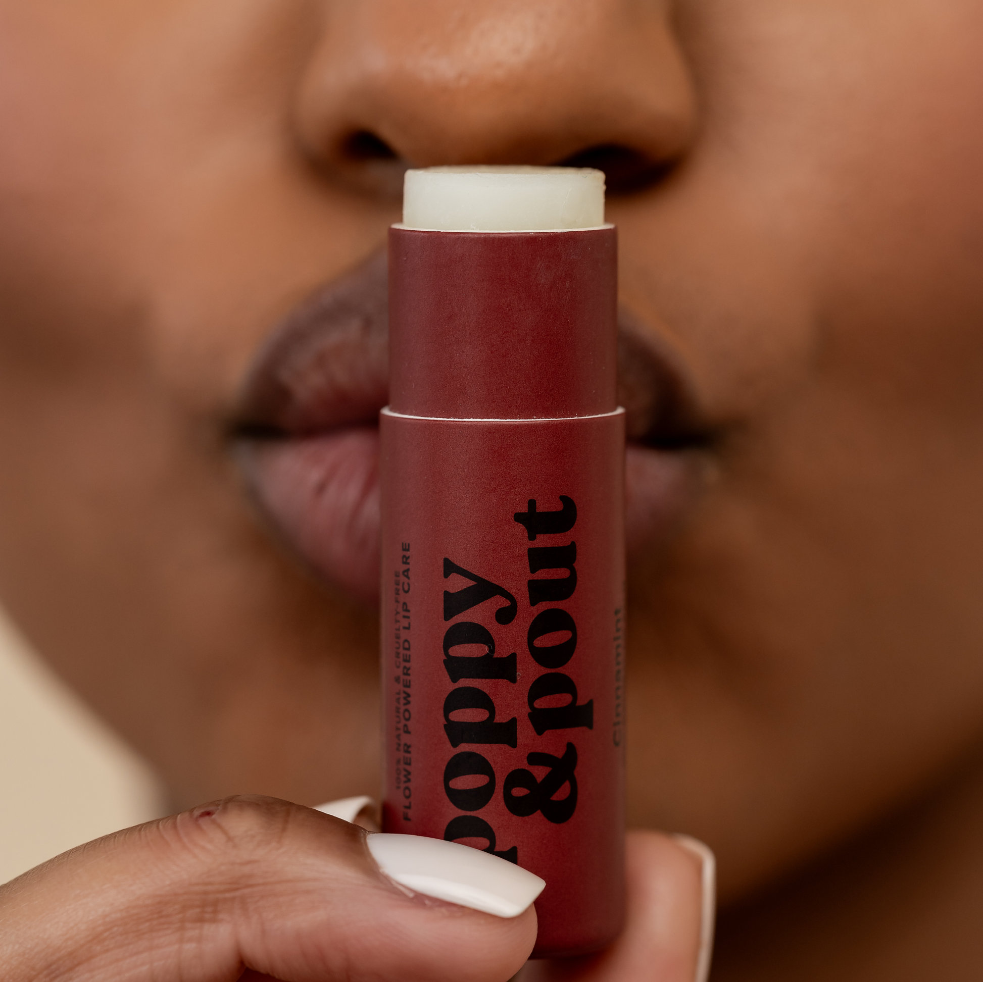 Lip balm stick with 'Poppy & Pout' branding held by a person.