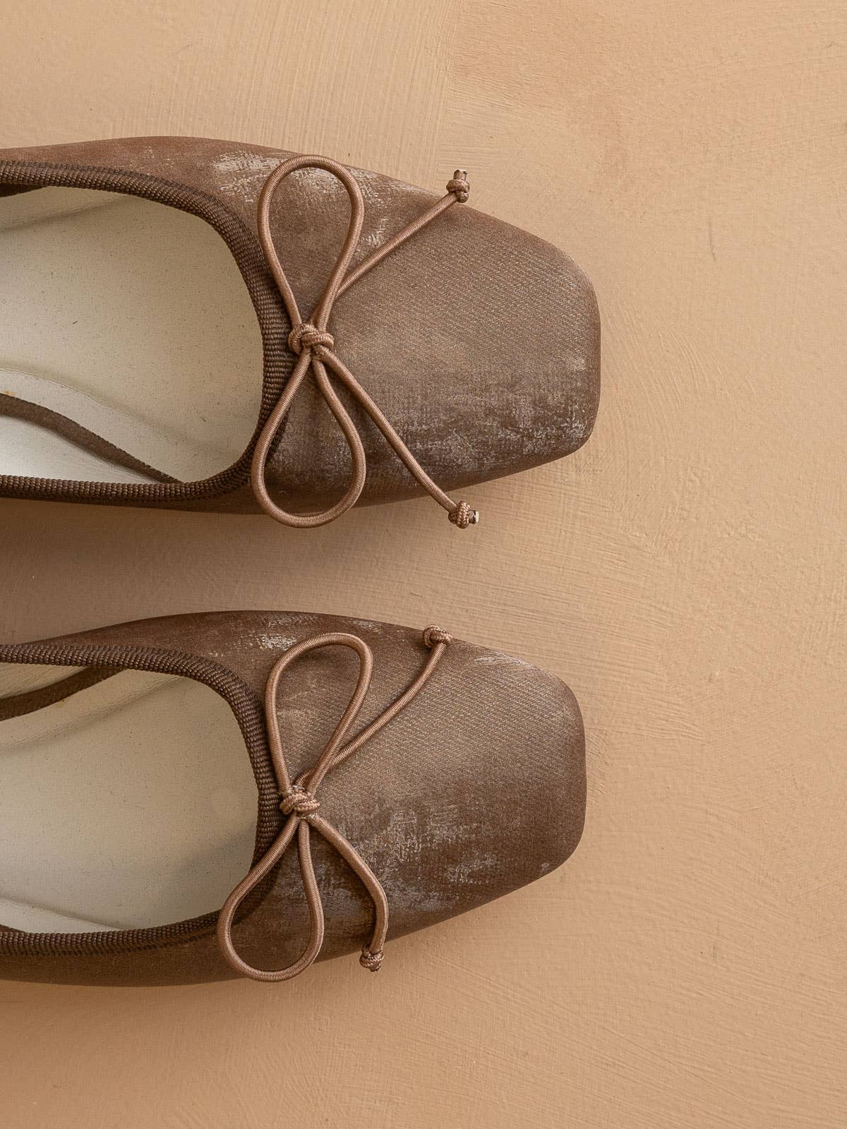 Top view of The London Ballet Flat by OASIS SOCIETY—a pair of brown square-toed slip-on flats with matching bows—perfect for everyday wear, displayed on a beige textured surface.